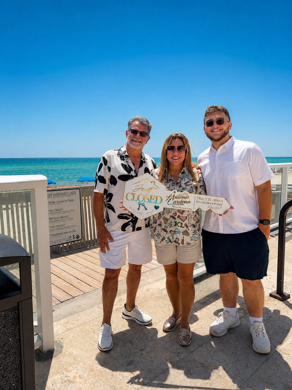 Tres personas en una playa soleada sostienen un letrero en forma de llave que dice Just CLOSED, con el logo de Antonio Cardona, el teléfono 786-731-9965 y @goldkeytony.